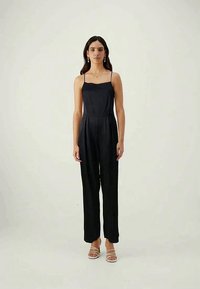 Mono negro con tirantes finos, corsé ajustado y piernas anchas. Textura suave, diseño sencillo y pliegues sutiles para un detalle adicional.