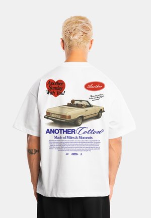 Persona con cabello rubio corto lleva una camiseta blanca con un coche antiguo y el texto "Another Sunday With You" en la espalda.
