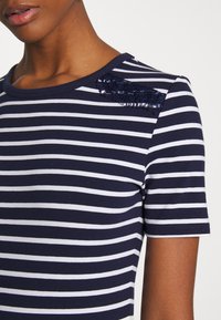 T-shirt w paski w kolorze granatowym i białym z okrągłym dekoltem, z koronkowym detalem na jednym ramieniu i krótkimi rękawami. Materiał mieszanki bawełny.