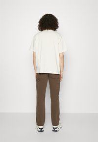 Vaalea beige puuvillainen T-paita rentolla istuvuudella, yhdistetty ruskeisiin cargohousuihin, joissa on sivutaskut ja suora lahjetyyli.