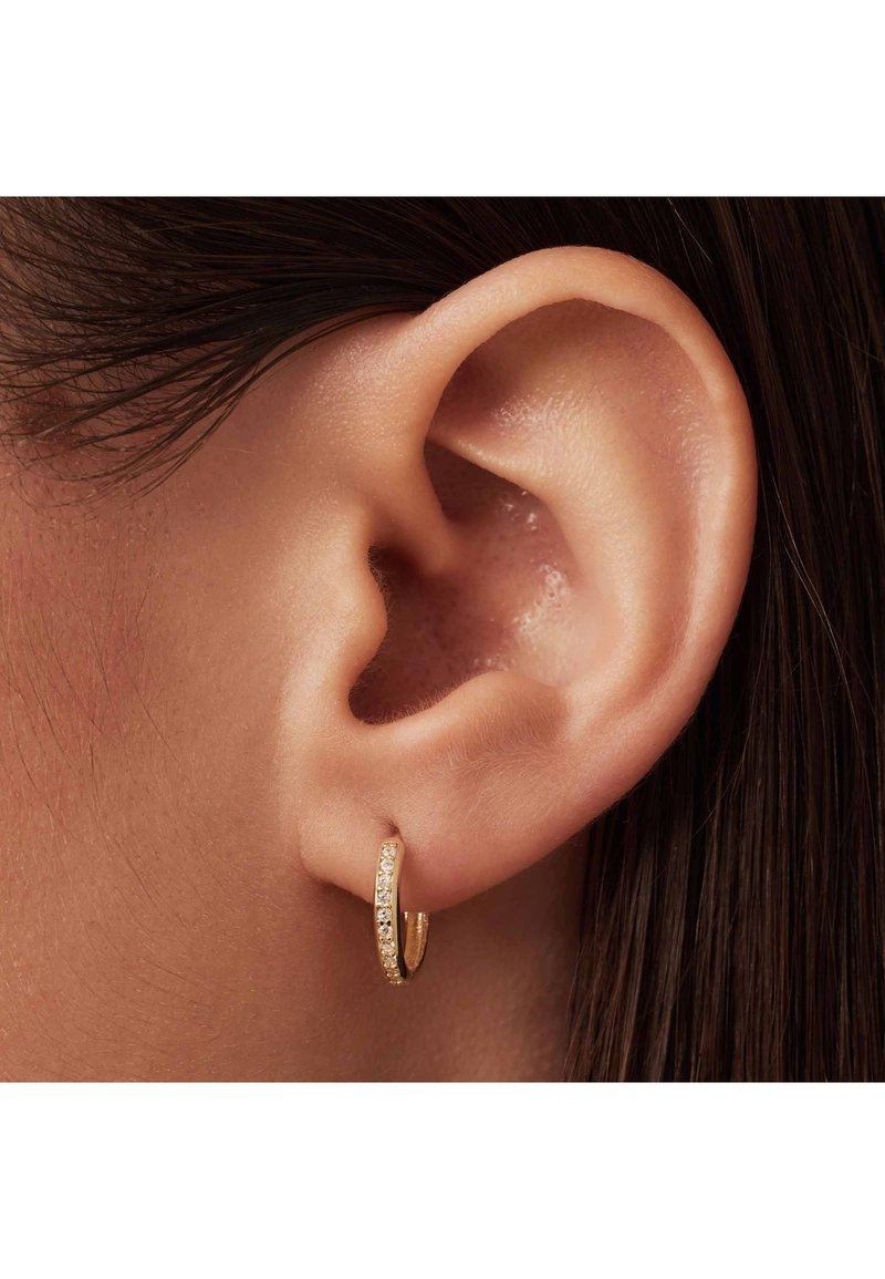 Gold hoop earring with a smooth, polished finish and a section featuring small clear gems. Worn in a pierced ear, showcasing its circular shape.