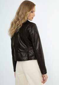 Zwarte leren jas met een getailleerd ontwerp, voorzien van een hoge kraag, zichtbaar gladde textuur en blootliggende ritsen op de mouwen.
