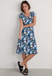 Lühikeste varrukate ja sinise lillemustriga kleit, millel on valged, kollased ja lillad detailid. V-kaelus ja põlvekohale ulatuv äär. Kanda mustade sandaalidega.