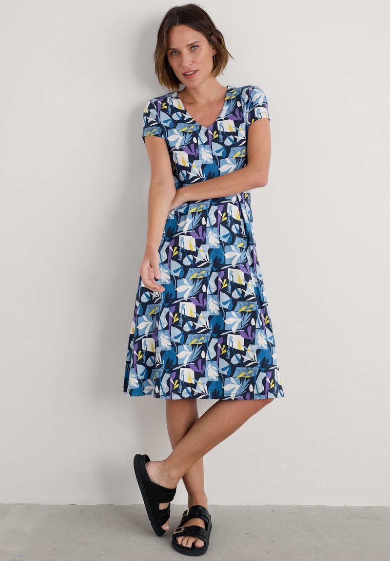 Lühikeste varrukate ja sinise lillemustriga kleit, millel on valged, kollased ja lillad detailid. V-kaelus ja põlvekohale ulatuv äär. Kanda mustade sandaalidega.