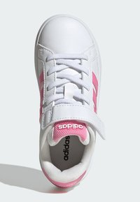 Vit lädersko med rosa detaljer, snörning och kardborreband. Texturerad innersula syns, märkt med "adidas" på tungan.