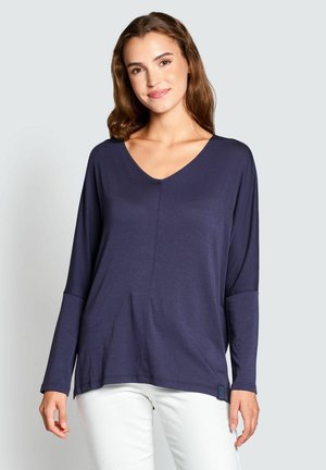 Navy long-sleeve V-neck top with a relaxed fit, featuring seam details and a tag on the lower left side. Soft, smooth texture.