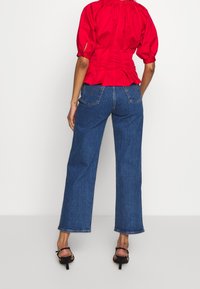 Röd blus med puffärmar och rynkad halsringning, parat med högmidjade, vida blå jeans i denim och svarta klackar med remmar.