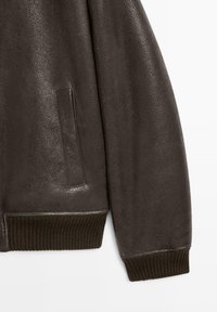 Mørkebrun læderjakke ærme og side, med en lodret lomme samt ribstrikket manchet og kant.