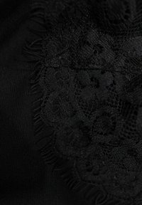 Tissu noir avec des détails en dentelle présentant des motifs complexes et des bords frangés, créant un contraste texturé contre un fond lisse.
