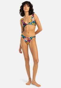 Blommönstrad bikini med triangeltopp och låg midja. Klara färger som rosa, gult och grönt på en svart bakgrund.