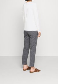 Weißes Langarmoberteil kombiniert mit taillierten Hosen in Marineblau und Weiß gestreift. Das Outfit wird durch braune Slidesandalen abgerundet.