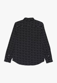 Chemise noire à manches longues avec un imprimé texte blanc répétitif sur l'ensemble. Dotée d'une fermeture à bouton aux poignets et d'un col classique.