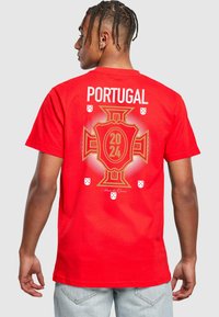 Raudona medvilninė marškinėliai, ant kurių yra užrašas "Portugal" ir grafika su skydu, metai "2024" bei maži balti skydo akcentai.