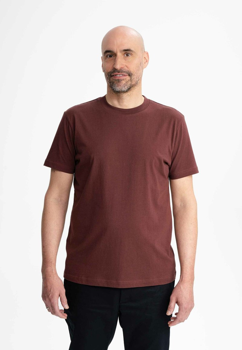 Bordeaux katoenen t-shirt met ronde halslijn en korte mouwen, weergegeven op een man met een neutrale achtergrond. Gladde textuur, geen patronen.