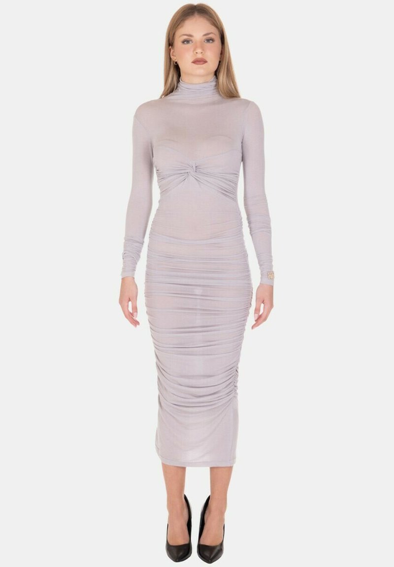 Abito fitted grigio chiaro con maniche lunghe, colletto a lupetto e dettagli arricciati in vita. Indossato con scarpe nere con tacco alto.