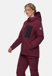 Bordeauxfärgad vattentät jacka med en svart bröstficka, justerbar huva och dragkedjefickor. Slät textur, designad för utomhusaktiviteter.