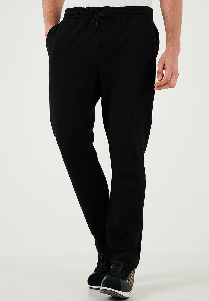 Zwarte sweatpants met een elastische tailleband, zijzakken en een losse pasvorm, gemaakt van een zachte, gladde stof.