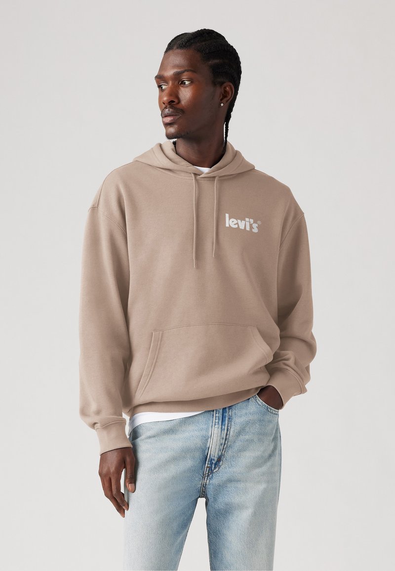 Haut à capuche beige avec une poche avant et un cordon de serrage, arborant un logo Levi's blanc. Associé à un jean en denim délavé. Texture douce.