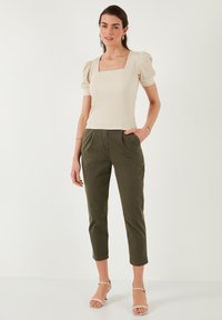Haut à manches courtes beige à rayures avec un col carré, associé à un pantalon vert olive court. Modèle portant des sandales blanches à lanières.