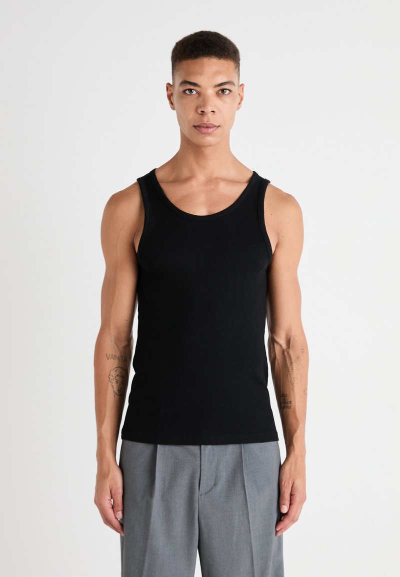 Débardeur en coton noir avec un col rond, design ajusté et texture côtelée, associé à un pantalon tailored gris clair.
