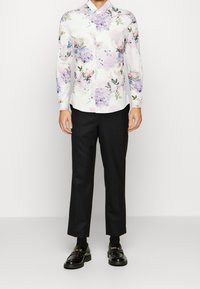 Kragenhemd mit floralem Muster in lila und rosafarbenen Tönen, kombiniert mit schwarzen Hosen und Loafers. Glatter Stoff mit taillierter Passform.