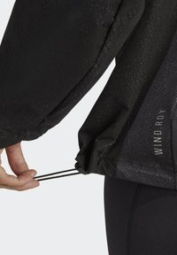Giacca a vento nera caratterizzata da una superficie testurizzata, regolazioni con cordino all'orlo e branding riflettente "WIND.RDY".