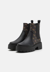 Botas Chelsea negras de tacón grueso con un panel lateral texturizado de patrón marrón, que cuentan con gomas elásticas y tiradores para facilitar el uso.