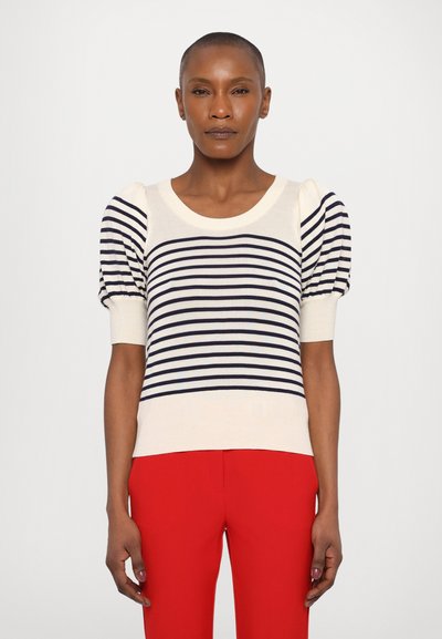 Un haut en tricot rayé présentant des rayures horizontales crème et marine, un col rond et des manches courtes bouffantes. Associé à un pantalon rouge vif.