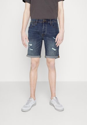 Jeansshorts in Dunkelblau mit Used-Effekten, umgeschlagenem Saum und klassischem Fünf-Taschen-Design. Kombiniert mit grauem T-Shirt und Sneakern.