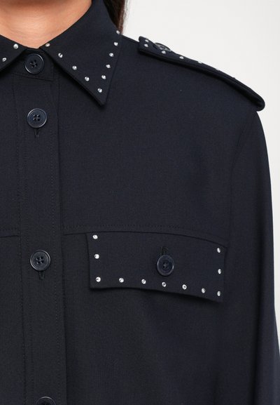 Navy shirt with a pointed collar, front buttons, and two chest pockets adorned with decorative silver studs and matching buttons on shoulders.