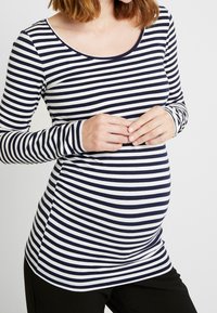 Långärmad amningströja med skopa i marinblå och vita ränder; gjord av mjukt material med en åtsittande silhuett och rundad nederkant.