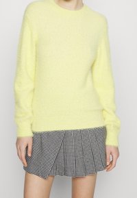 Żółty, puszysty, dziergany sweter z długimi rękawami, zestawiony z dopasowaną plisowaną spódnicą w czarno-biały wzór pepitki. Miękka tekstura, okrągły dekolt.