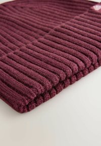 Berretto lavorato a maglia bordeaux con texture a costine verticali, dotato di un risvolto e realizzato in materiale morbido simile alla lana. Nessun marchio o motivo visibile.