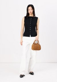 Top sans manches noir à côtes avec fermeture à boutons sur le devant, associé à un pantalon large blanc et un sac à main matelassé beige. des ballerines noires à bout pointu.