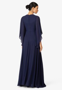 Abito lungo blu navy con maniche a falda trasparenti, busto aderente e gonna fluida. Chiusura con zip sul retro per una facile vestibilità.