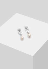 Pendientes de plata con un diseño circular martillado, adornados con una única perla de color crema, que muestra una textura suave.
