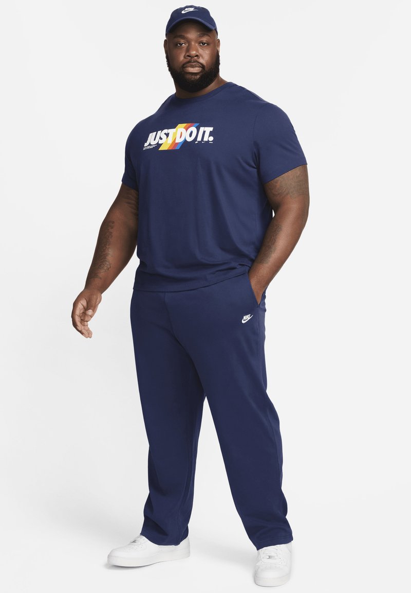 Ensemble de sport marine composé d'un T-shirt avec l'inscription "JUST DO IT." imprimée en texte multicolore et d'un pantalon assorti. Accents du logo Nike en blanc.
