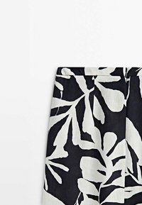 Zwarte stof met groot wit bloemmotief. Heeft een rechte snit en een ritsdetail aan de achterkant. Glad, textuurafwerking.