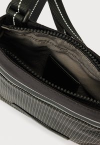 Fekete keresztpántos táska fehér kockás mintával, a nyitott fő cipzár finom szürke belsőt és kis belső zsebet tár fel.