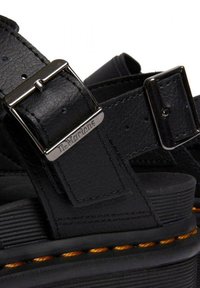 Sandalias de cuero negro con correas ajustables, hebillas de metal y superficie texturizada. Cuentan con una suela de goma gruesa con costuras naranjas en contraste.