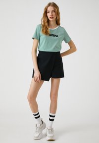 Grønstribet t-shirt med sort "GRATEFUL" tekst, parret med sorte shorts. Tilbehøret inkluderer hvide sokker med sorte striber og sneakers.