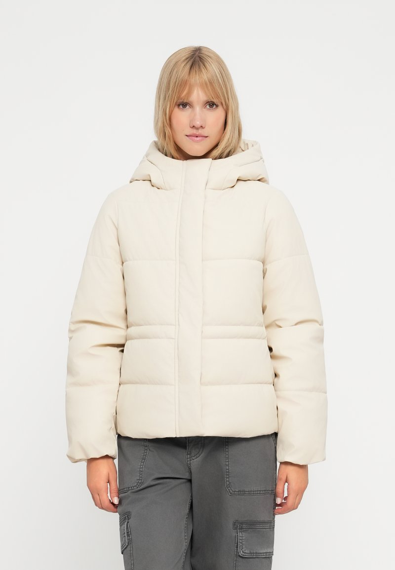 Puffjakke i lys beige med quiltet design, høj krave og hætte. Materialet ser glat og let blankt ud.