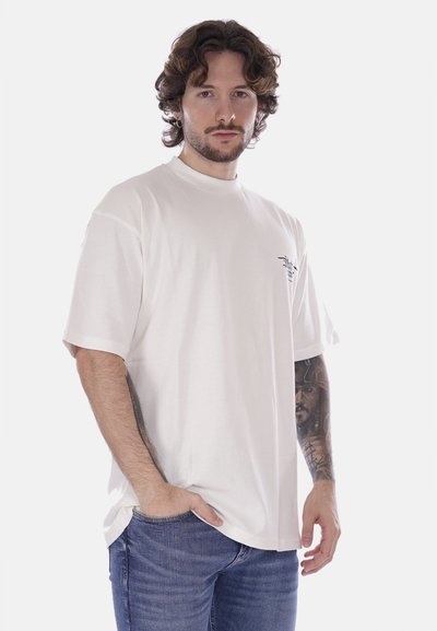 T-shirt bianco in cotone con maniche corte, collo rotondo e vestibilità ampia. Presenta una piccola grafica nera sulla parte sinistra del petto.