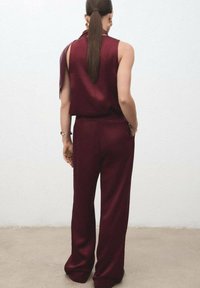Bordeaux satijnen twee-delige outfit met een mouwloze top en wijde broek. Glad textuur, aansluitende taille en minimalistisch ontwerp.