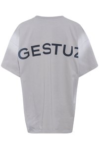T-shirt in cotone grigio con taglio ampio e spalle scese. Sul retro è presente la parola "GESTUZ" in caratteri maiuscoli, di colore blu scuro.