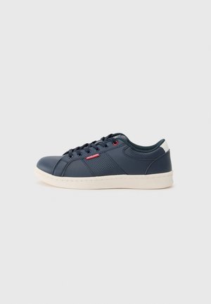 Navy blue low-top sneaker with white sole, lace-up front, perforated side panel, and red "Jack & Jones" tag on neutral background.