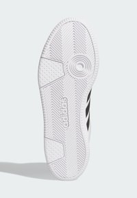 White rubber shoe sole with textured grip patterns, featuring a prominent circular detail and the 'adidas' logo in black.