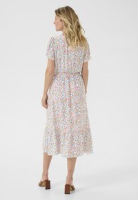 Blommig midiklänning med korta puffärmar, elastisk midja och flödande nederkant. Framträdande vit bakgrund med färgglada blommönster.