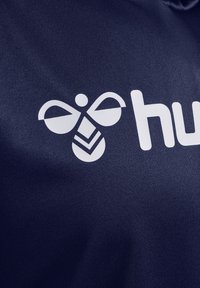 Navy stof toont een wit logo met een gestileerde bij en geometrische accenten onder het woord "huh." Textuur oppervlak.