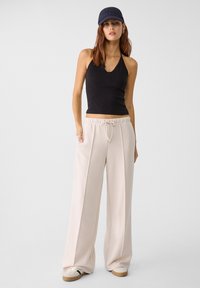 Černý halter top v kombinaci se světle béžovými širokými kalhotami s elastickým pasem a šňůrkou. Bílé tenisky s hnědým podrážkou.